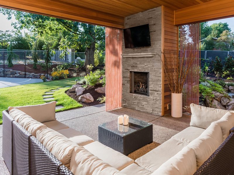 A covered outdoor patio with a wall-mounted TV over a fireplace
