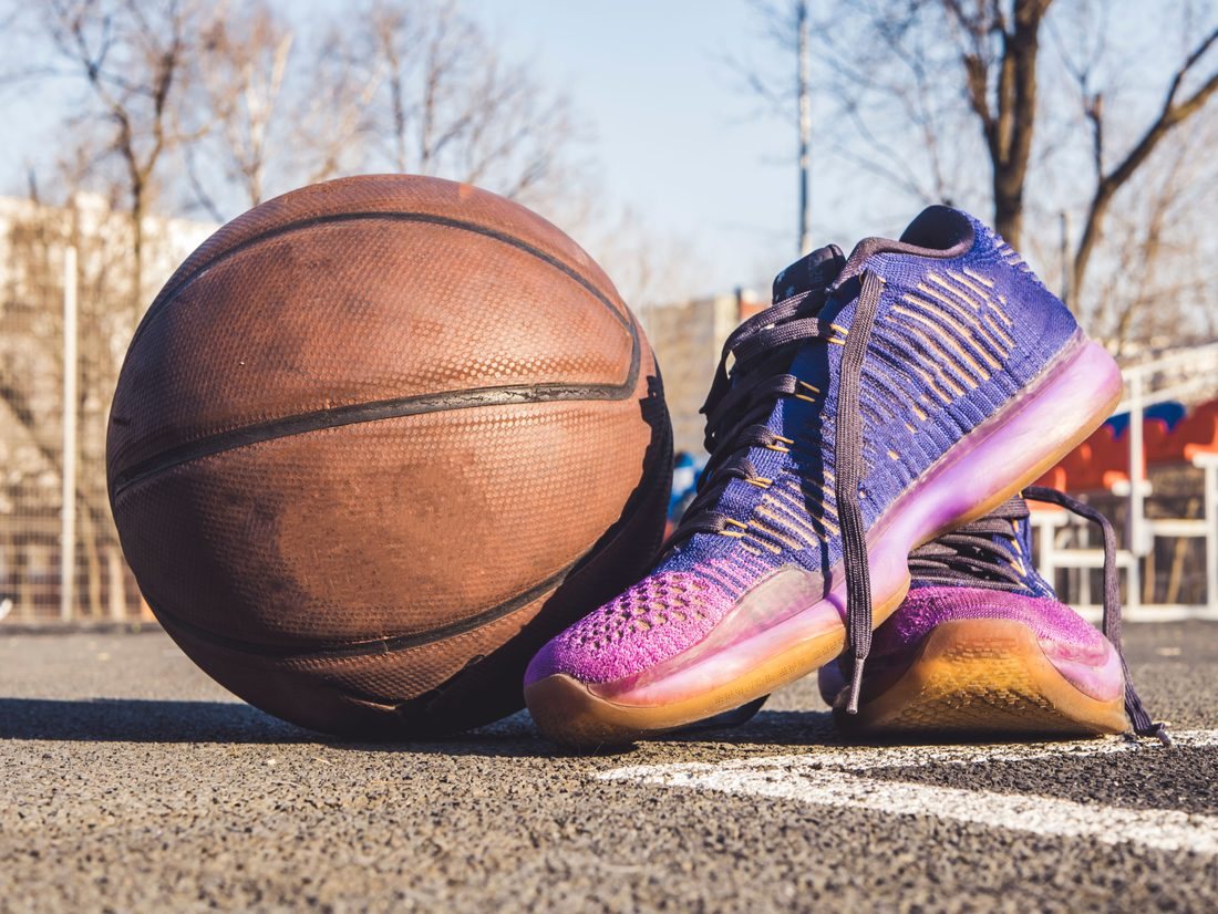Pair of basketball shoes beside a basketball on an outdoor court