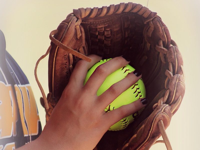 A hand holding a softball inside a leather glove